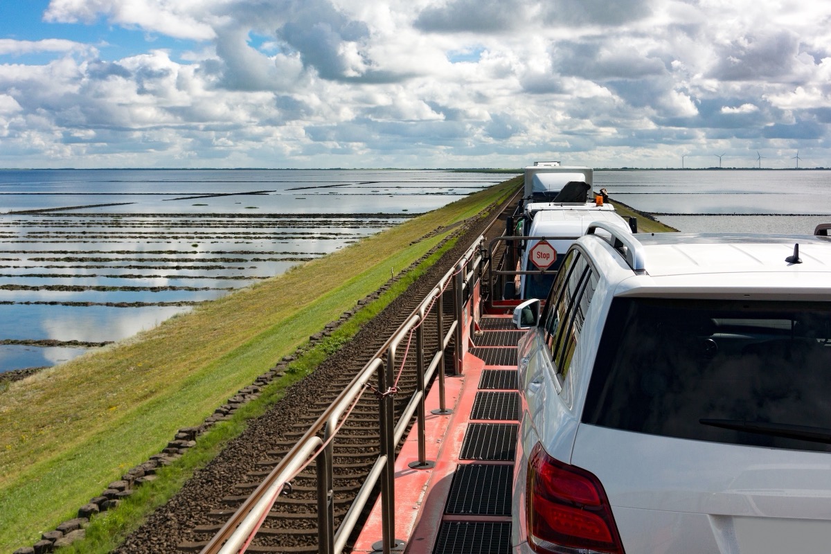 Autozug auf dem Hindenburgdamm nach Sylt: verladene Autos auf dem offenen Tragwagen, daneben das Wattenmeer